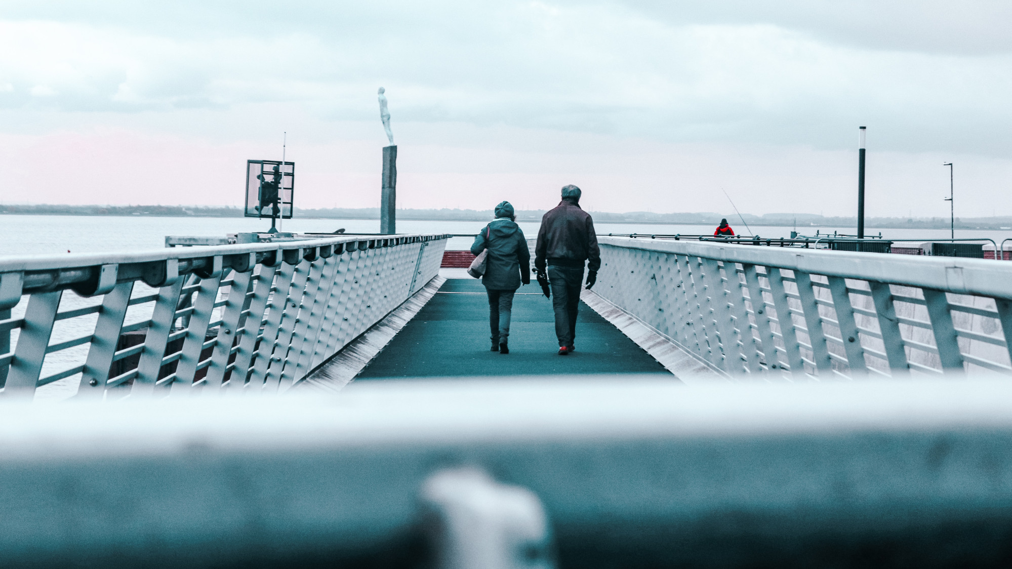 Two people walking off into the distance on a bridge
