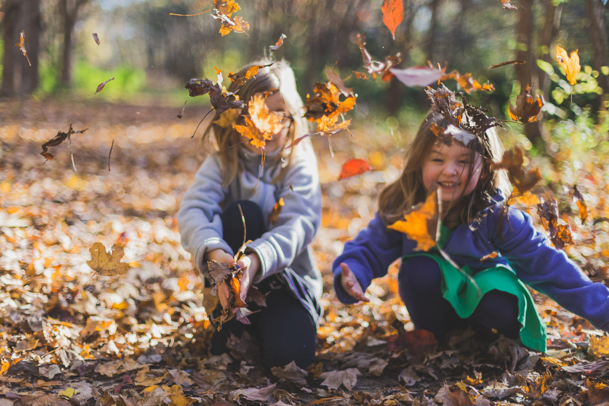 Two young girls bent down playing in the autumn leaves
