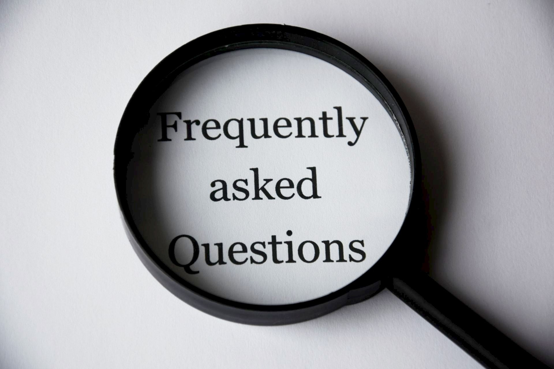 Plain white background with a magnifying glass showing the words frequently asked questions