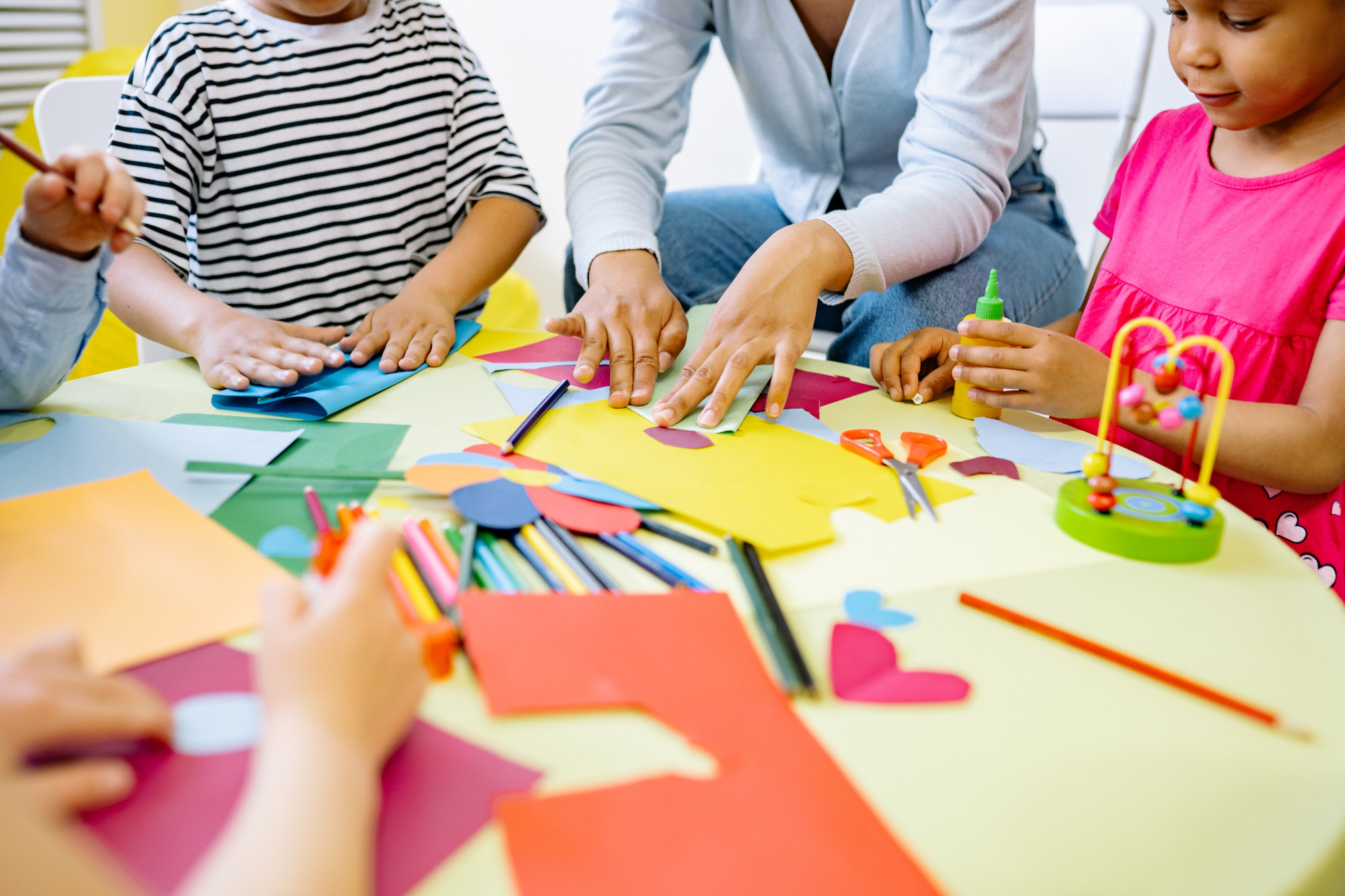 Children and a teacher sat around the table being creative with lots of coloured paper and pens 